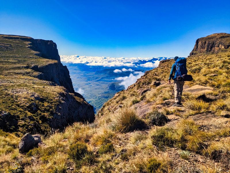 hiker walking on a mountain with clouds in the distance