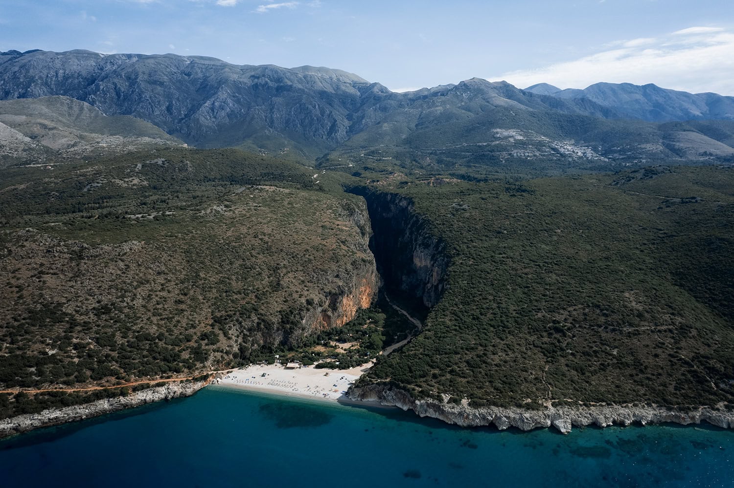 an aerial view of a white sand cove amongst cliffs in Albania