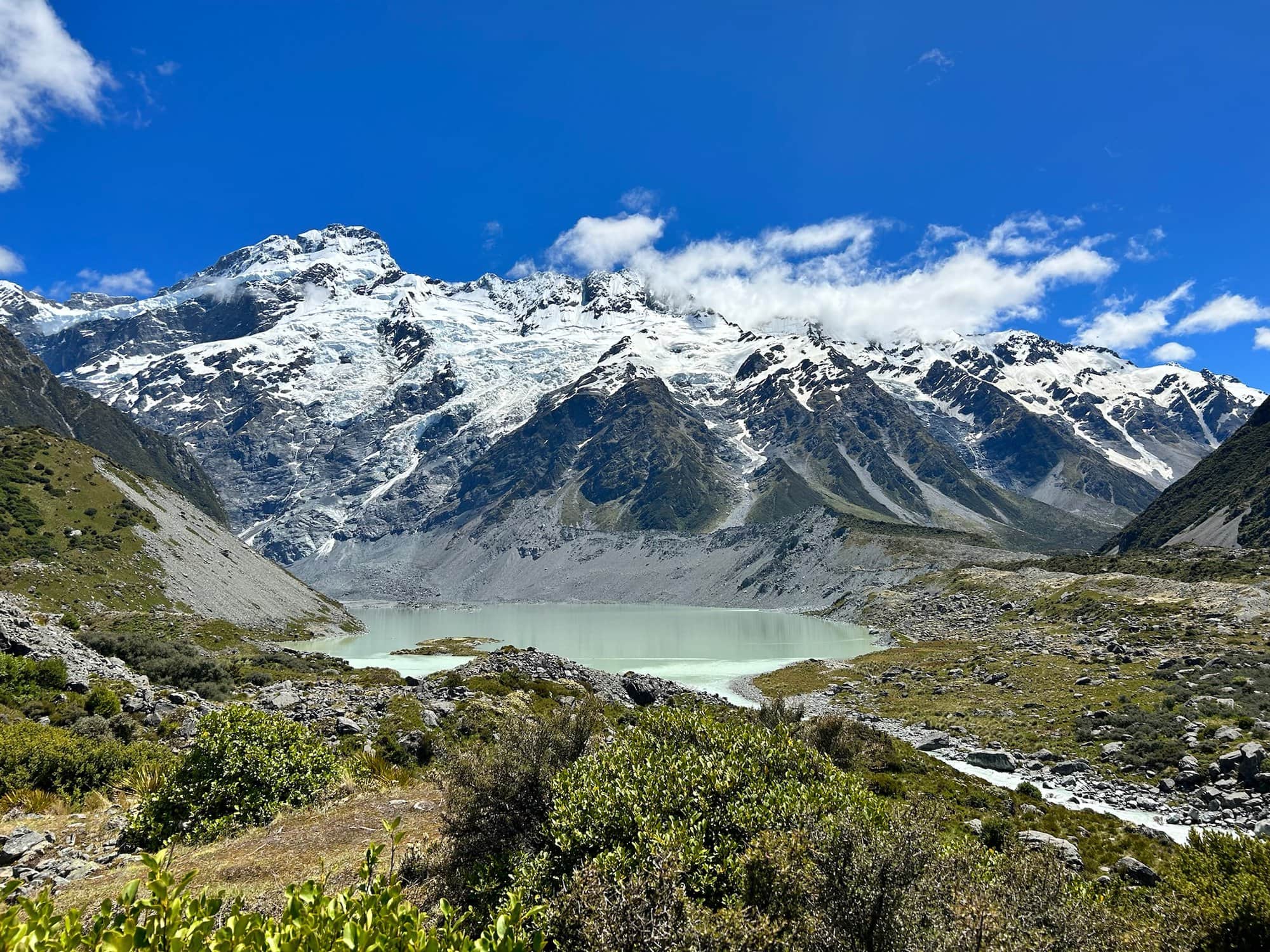 View from the Hooker Valley trek near Mount Aoraki of snow capped mountains surrounding an icy blue crater