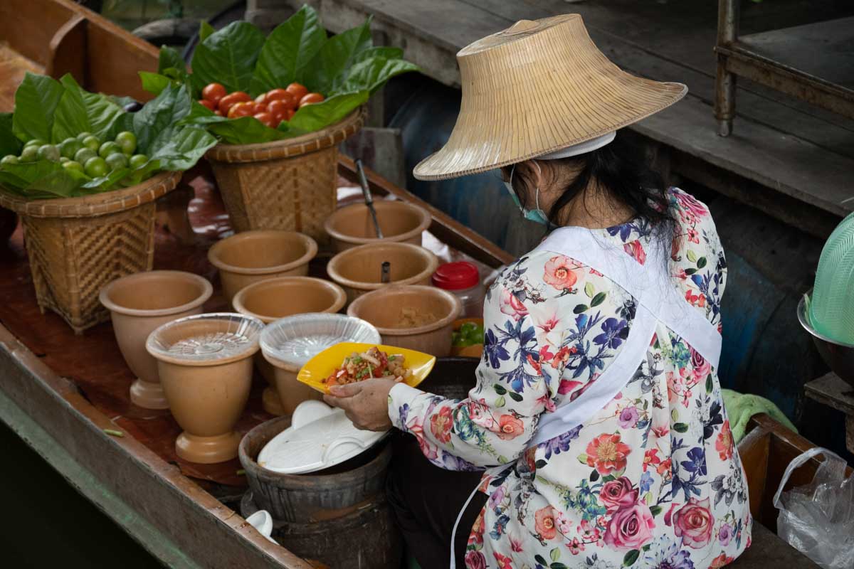 a thai lady on her boat selling food at a floating market in thailand