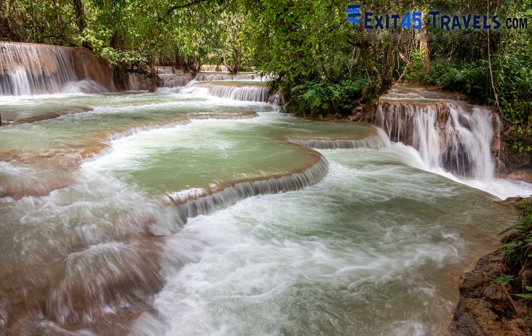 green coloured water flowing over rocks downstream from a waterfall - Laos is one of the best countries to visit in January