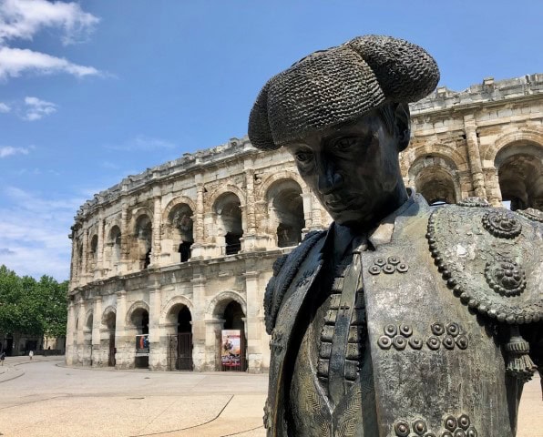 Roman amphitheater in Nimes with a bronze statue of a man in the forefront