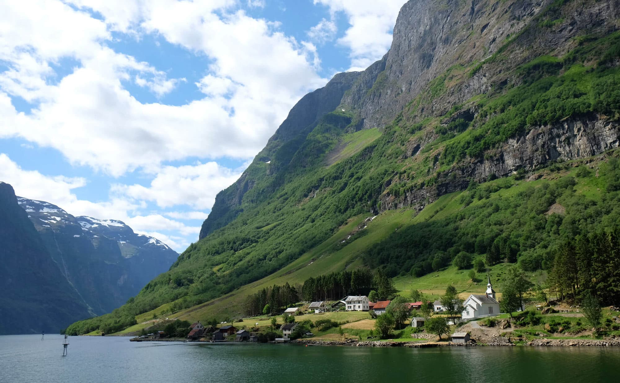 a small town on a lake with a large green mountain behind