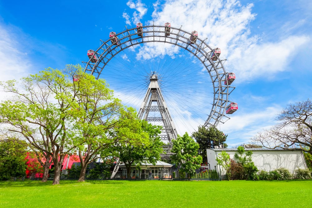 a large ferris wheel in a park with green grass at forefront