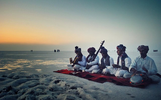 4 indian musicians sitting on a mat in the desert