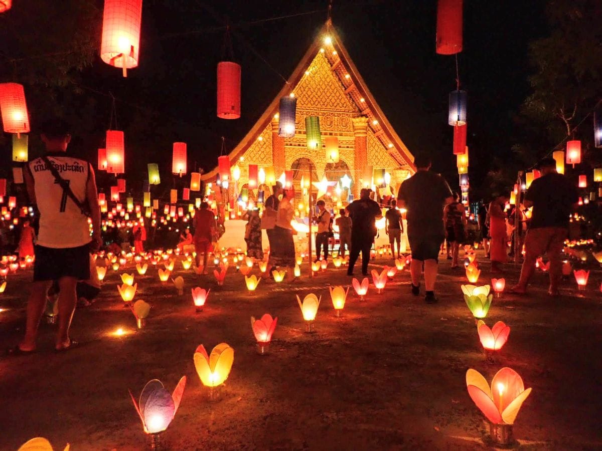 Candles and paper lanterns lit up at night leading to a temple in the background