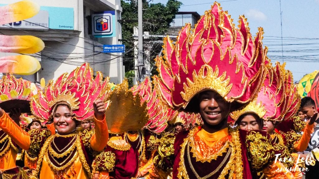 men and women in a street parade in the philippines dressed in orange and red with big head dresses