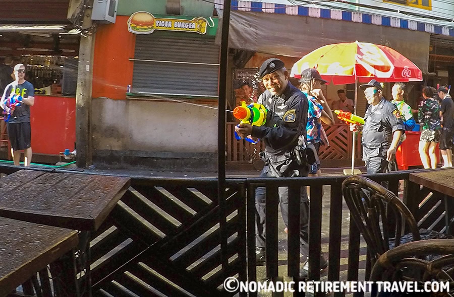 thai police man in uniform with a super soaker water pistol shooting it into the crowds
