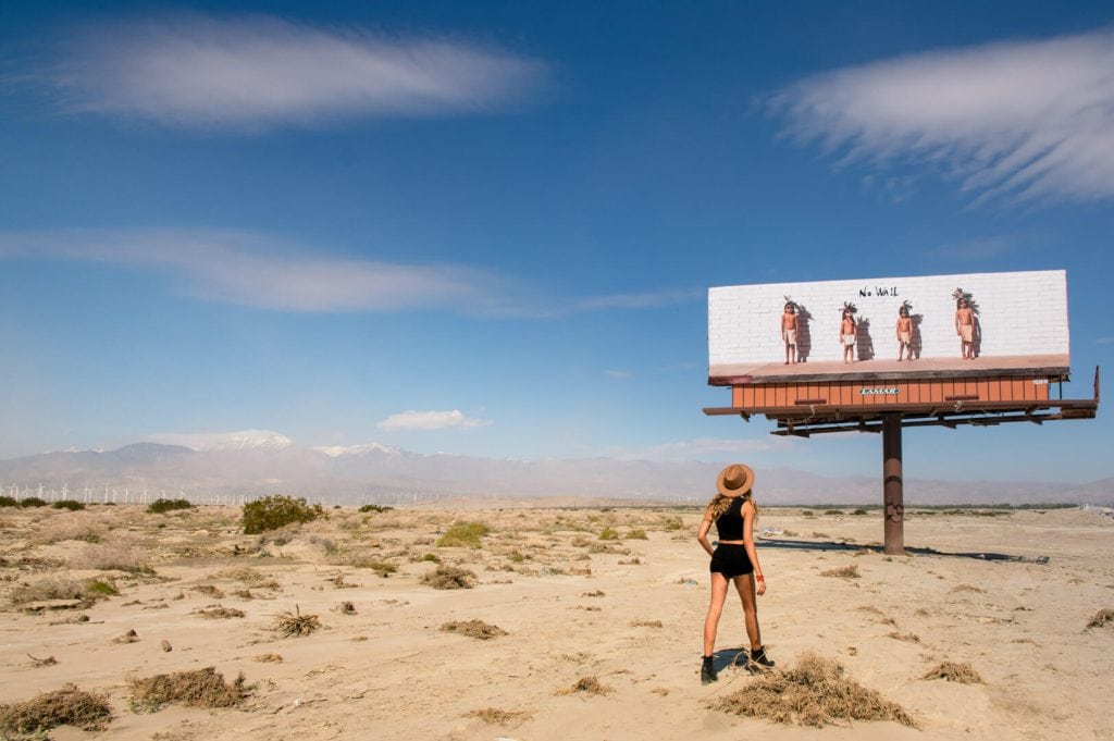 a woman standing in the desert looking at a billboard