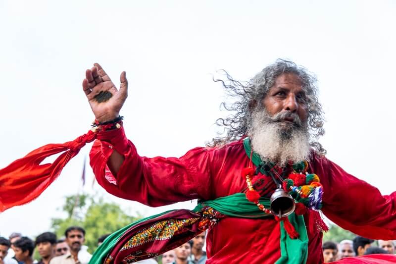 a man dressed in red with a long grey beard - the dhamal performance at the March Festival of mela chiraghan