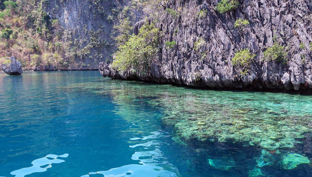 crystal clear aqua water with limestone karst mountains above and below the water line