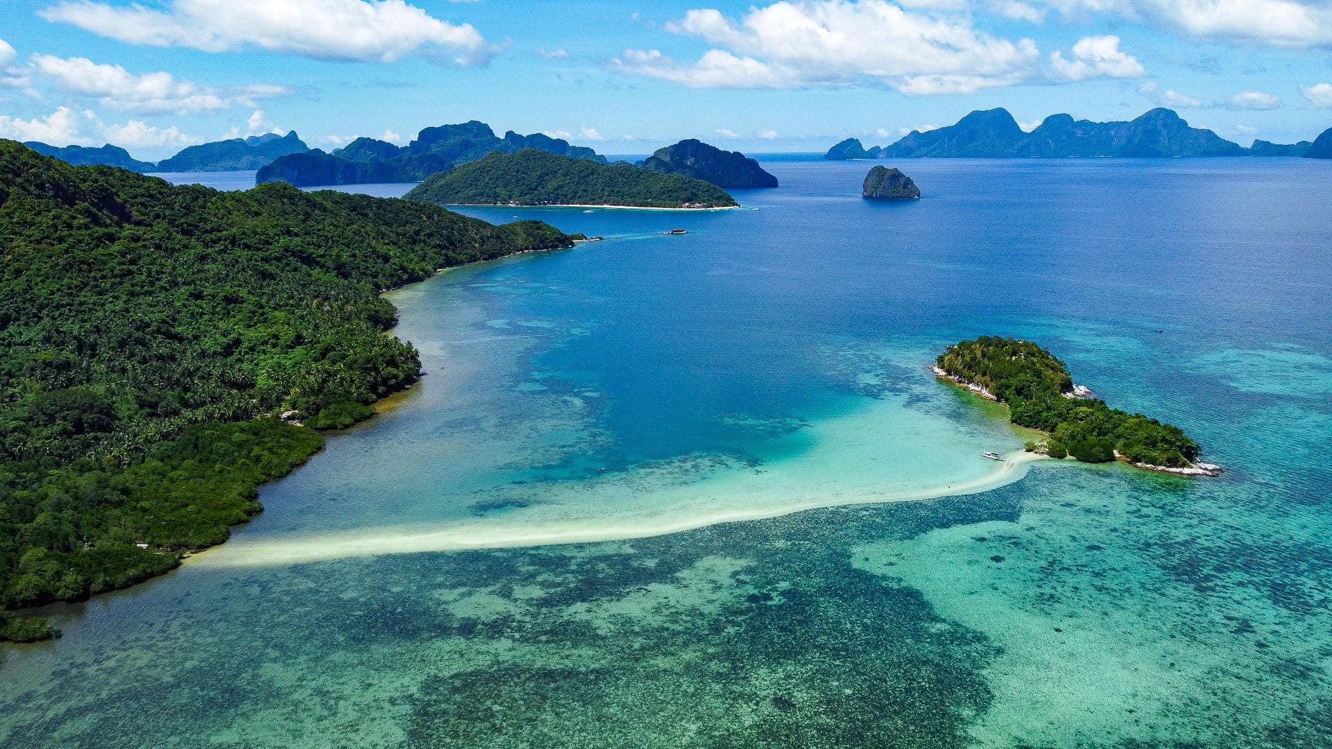 long thin white sand sandbank in crystal clear waters surrounds by smaller islands