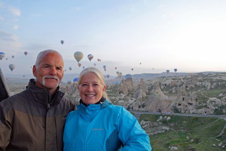 a couple standing in front of lots of hot air balloons in the sky in Cappadocia, Turkey
