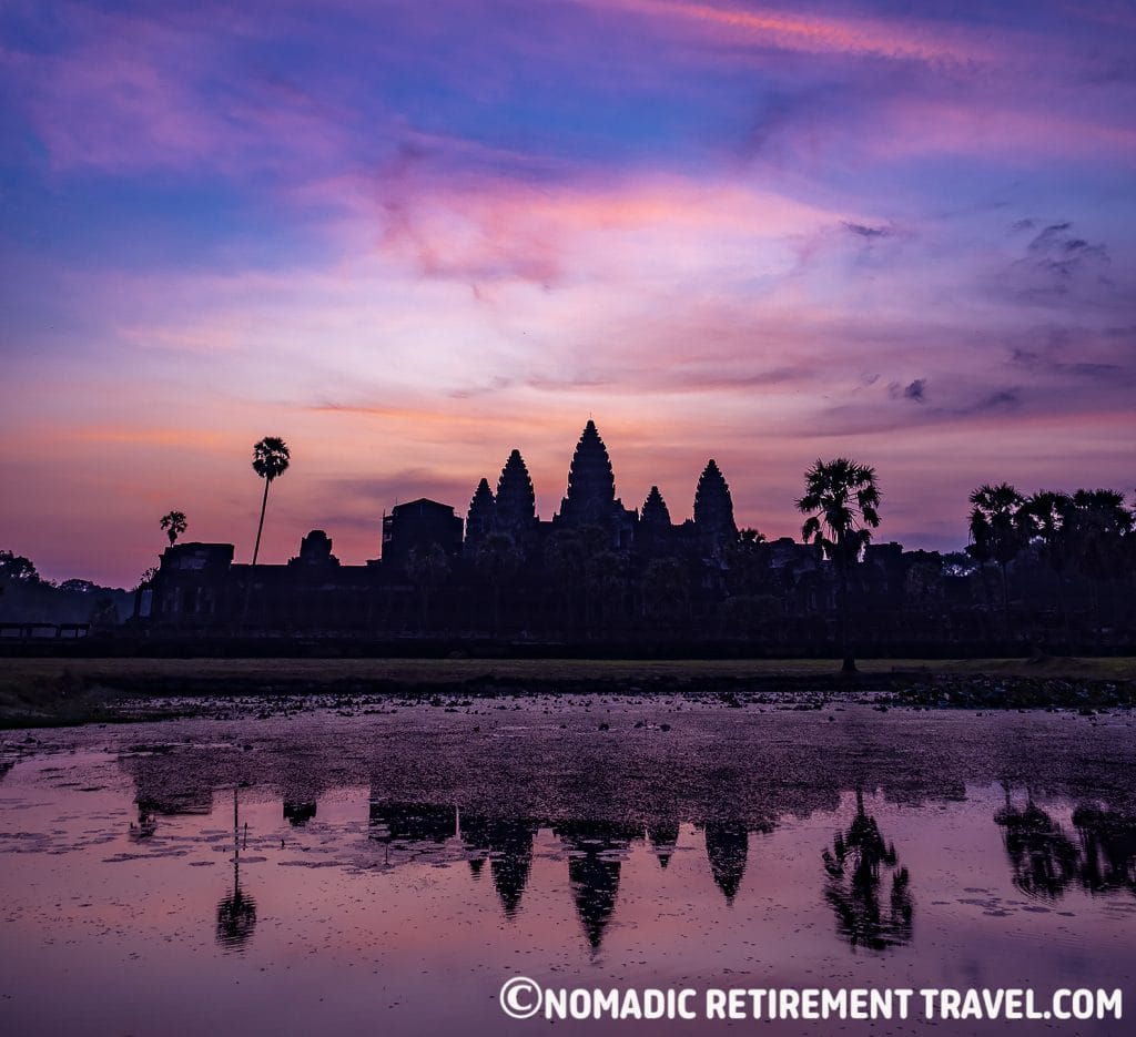 the ruins of angkor wat reflected in water at sunrise with the sky in pinks and purples