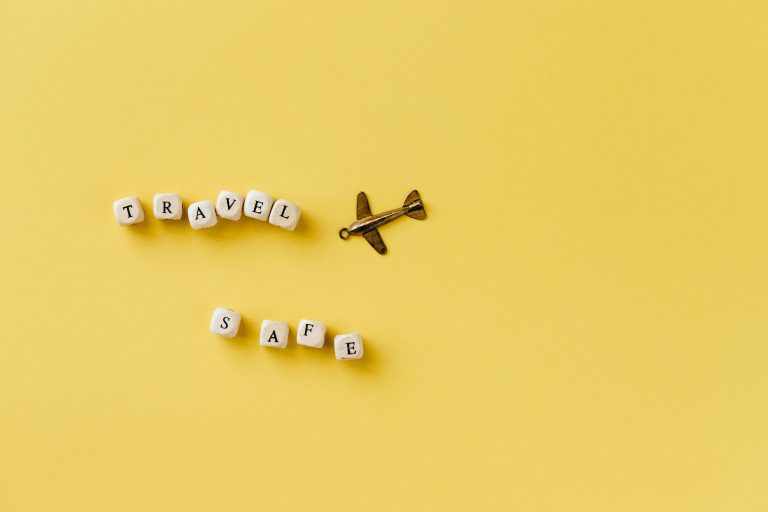 the words 'travel safe' spelt out in wooden blocks with a toy plane n a yellow background