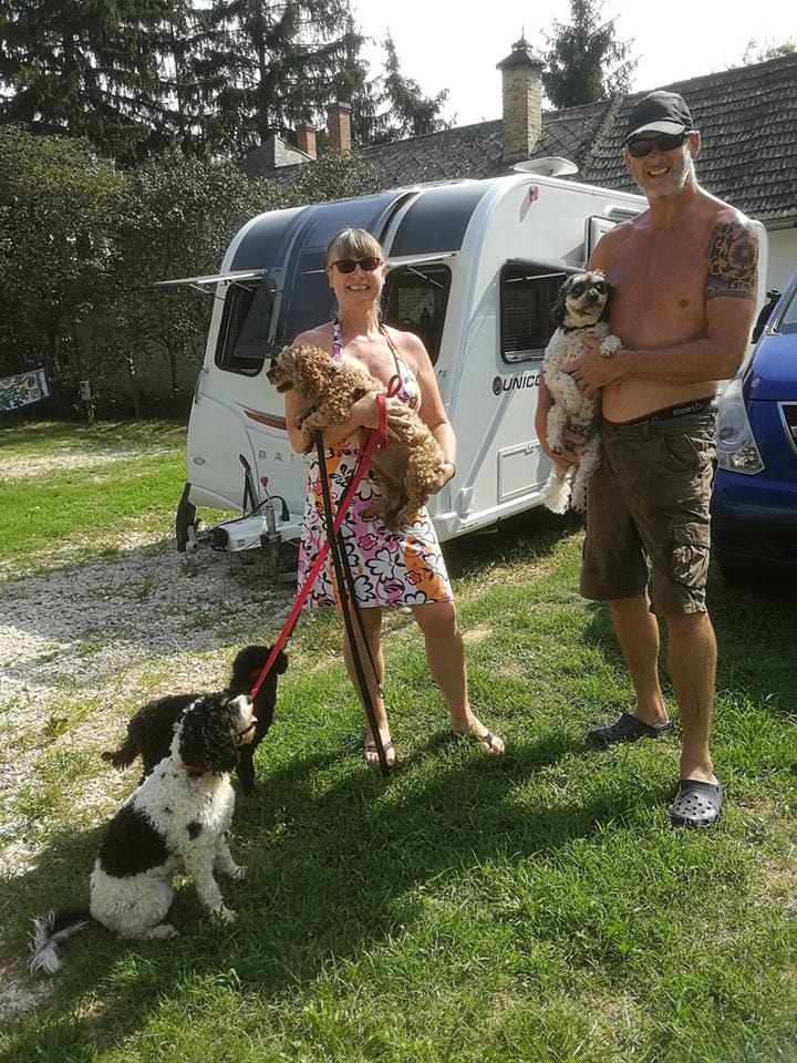 a couple with 4 dogs standing in front of a caravan