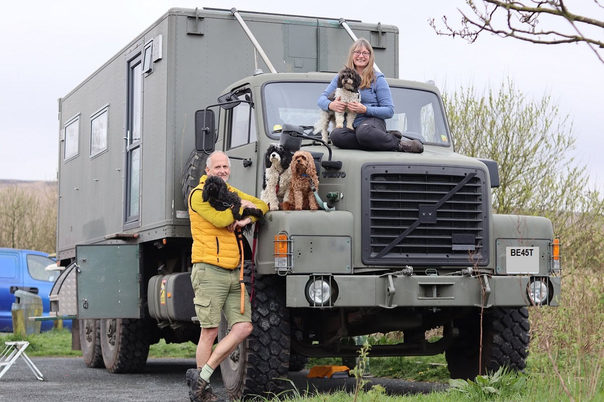 a truck with a man standing beside and a woman on the bonnet with 4 dogs
