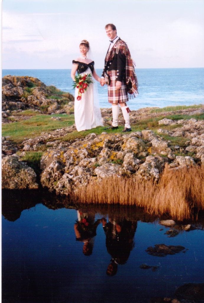 a couple dressed in scottish wedding gear standing on rocks at their wedding