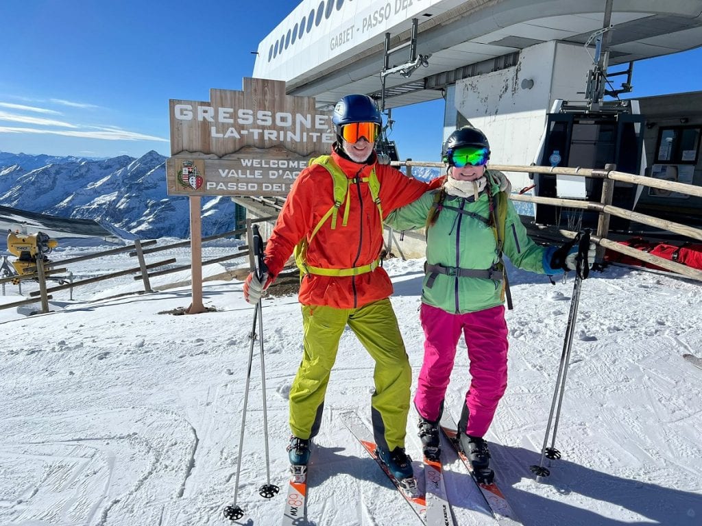 a couple in bright ski gear standing in front of a ski lift