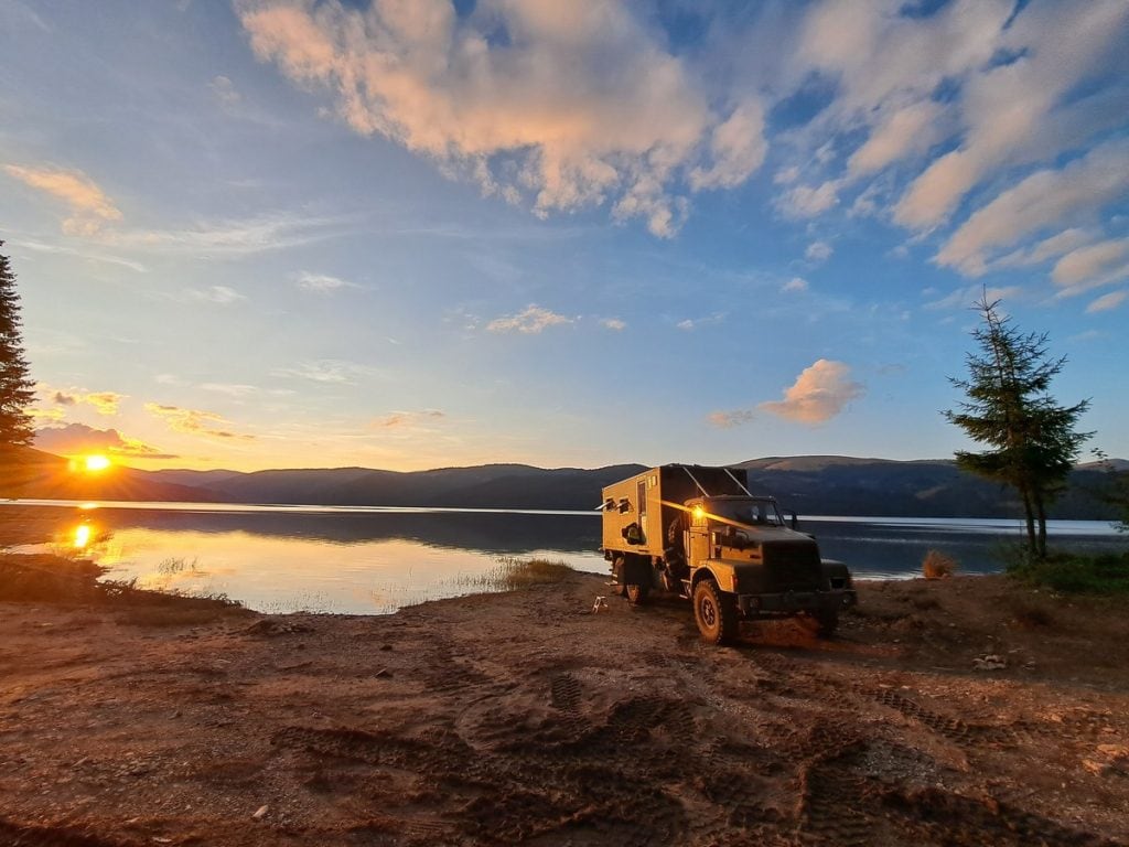 a truck on the edge of a lake as the sun sets