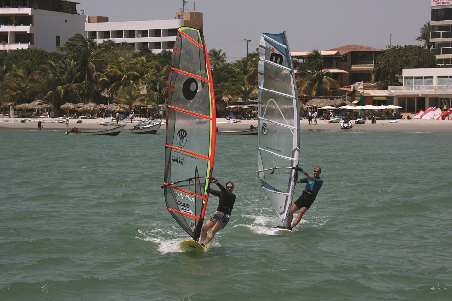 a man and woman windsurfing off the coast with land in the background
