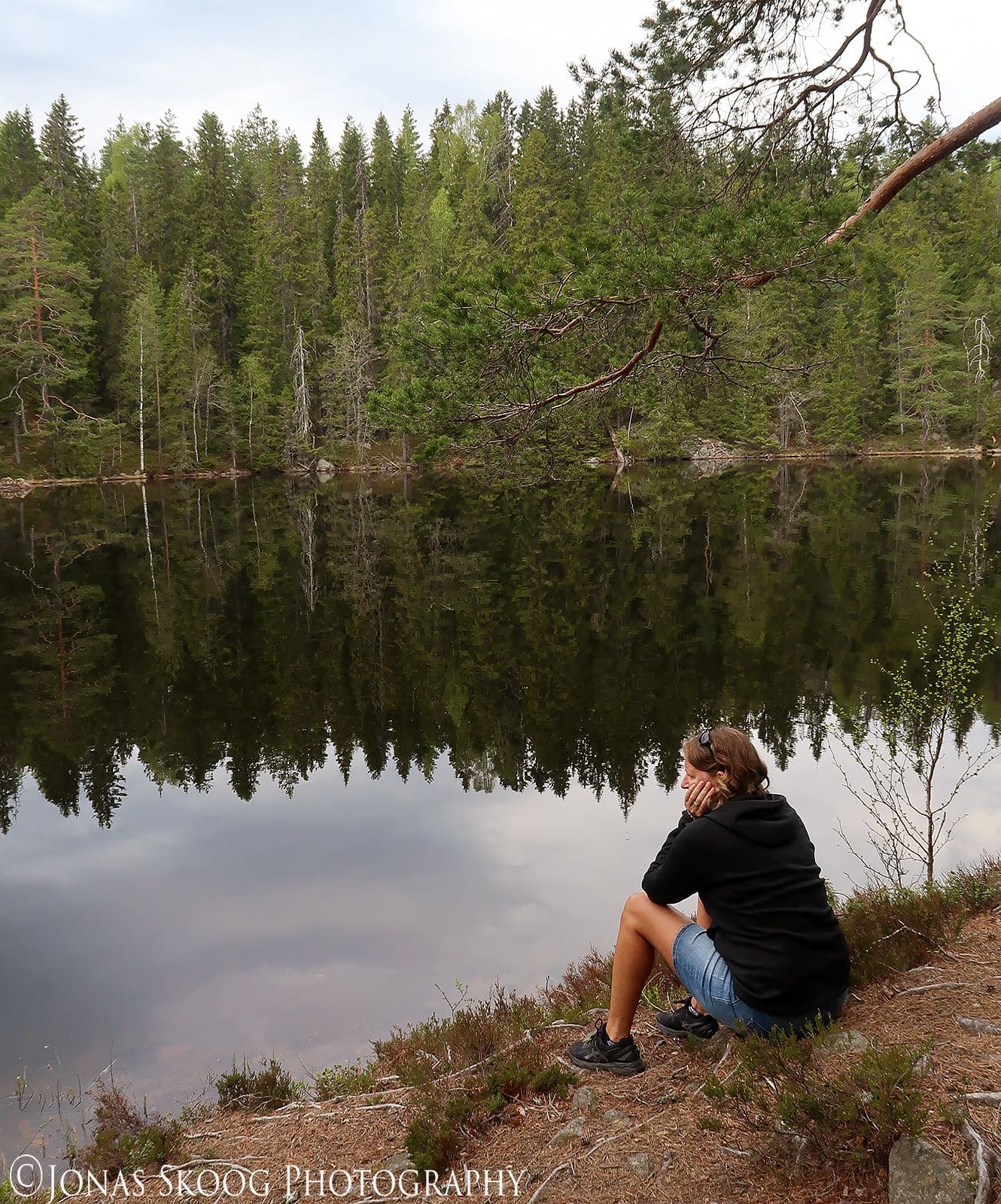 Woman sitting alone by a lake looking reflective