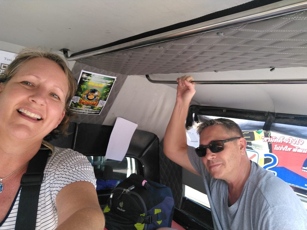 Nomadic travel couple riding in an open-air taxi truck with luggage during a travel day transfer.