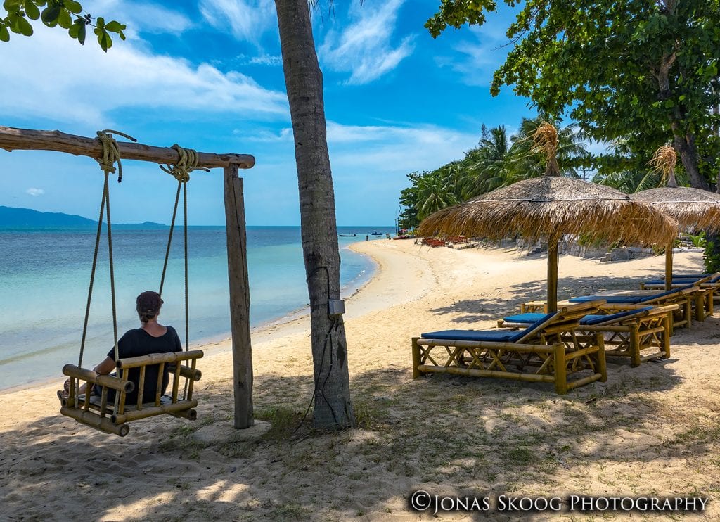 Woman sitting on a wooden swing overlooking a tropical beach in Koh Samui Thailand
