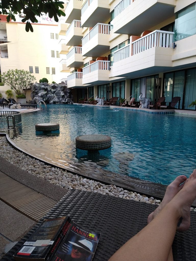 Person relaxing and reading a book by a hotel pool